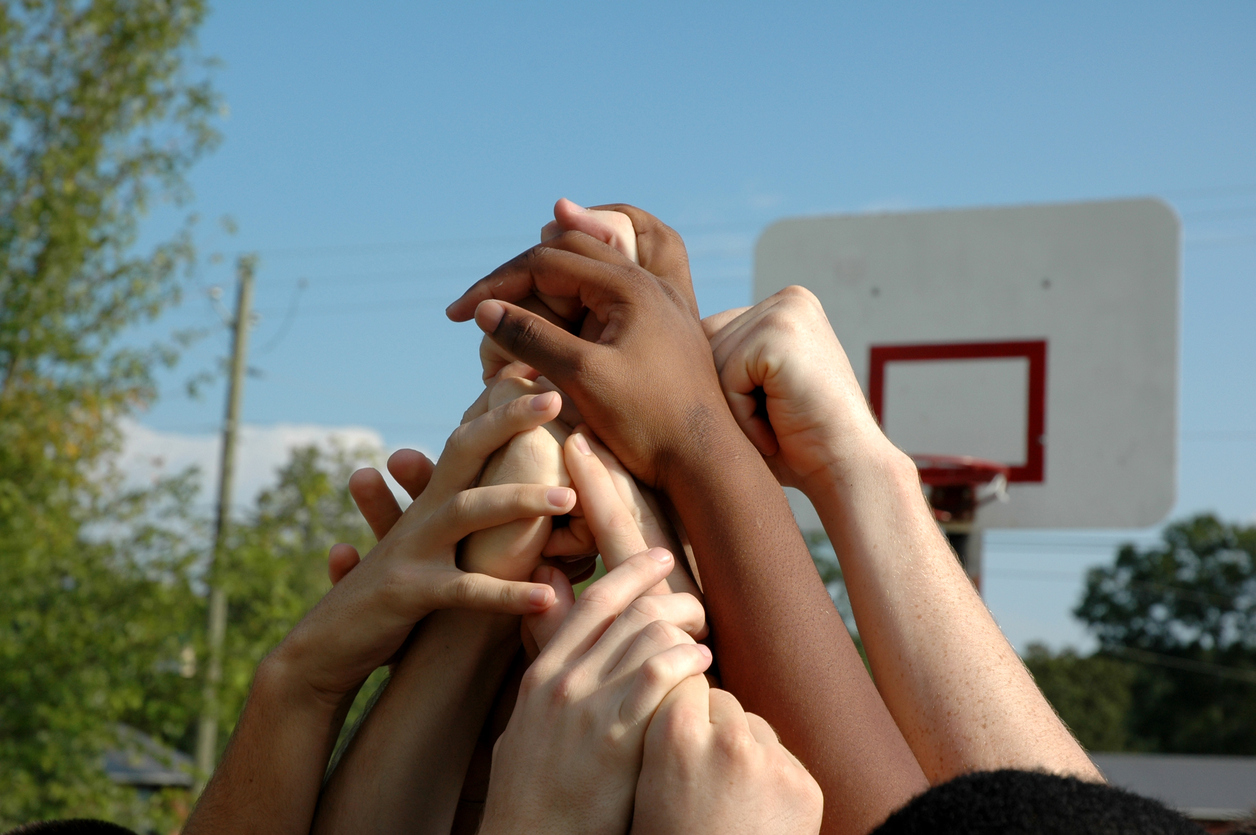 A team raises its hands around a huddle after a victory.